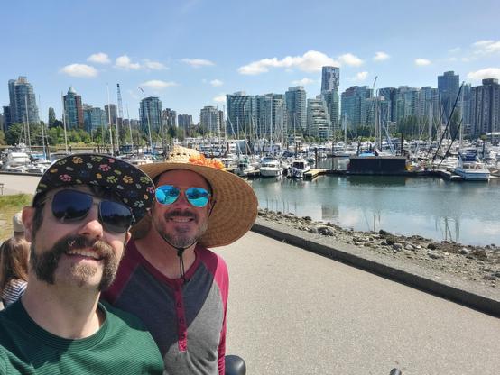 My husband and me posing in front of sailboats parked in a pier with some of the Vancouver skyline in the background. Many of the buildings have a similar style of tall glass exteriors.