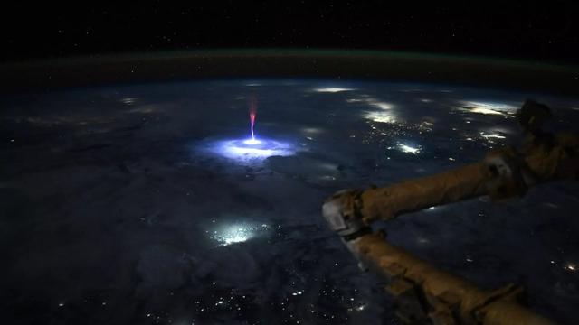 La Terre vue depuis l'espace de nuit avec au centre de l'image un éclair qui va du rose au bleu/blanc frappe la haute atmosphère et là où il "touche" les nuages on voit se former 2 énorme cercle bleu/blanc concentrique très lumineux… le tout pris depuis l'espace (donc on voit la rotonduité de la Terre de nuit et c'est trop beau) avec un bras mécanique au premier plan.