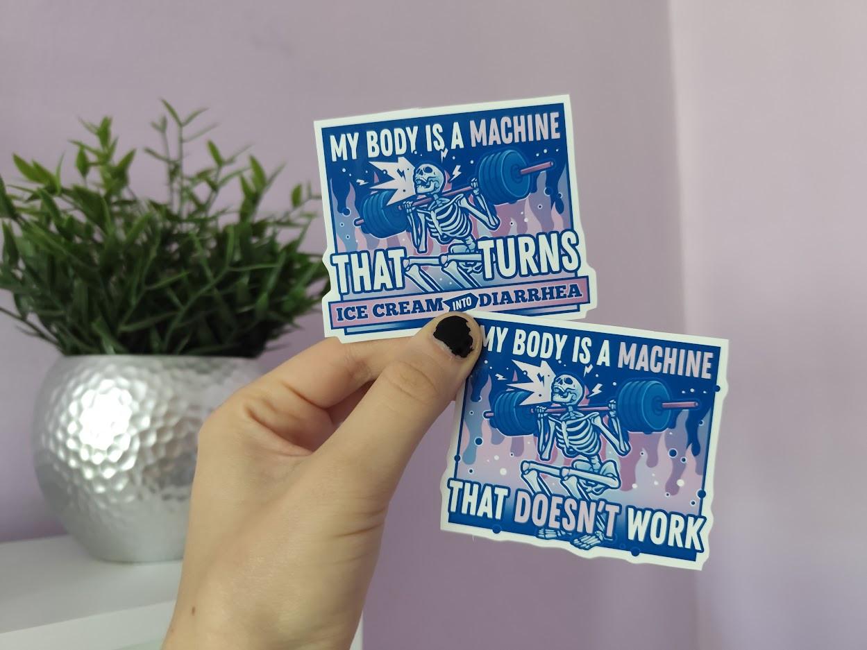 Hand holding up two stickers of a skeleton lifting a heavy weight, titled "my body is a machine that turns ice cream into diarrhea" and "my body is a machine that doesn't work"