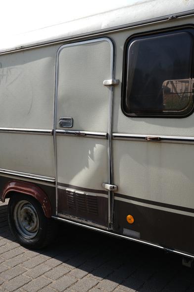 Seitenansicht eines 1982er Wohnwagens Eriba Troll. Die Tür ist deutlich verbeult, nachdem ein Transporter gegen gefahren ist.