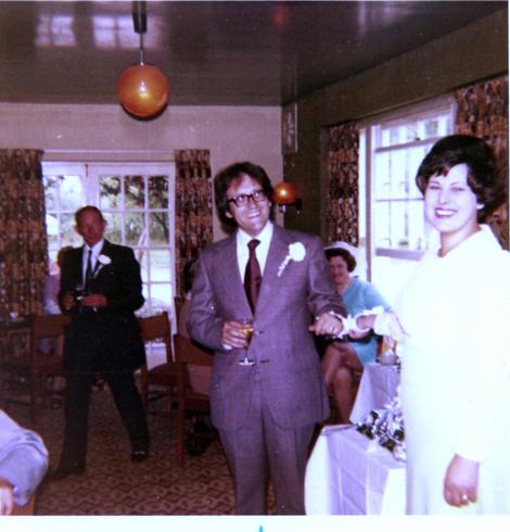 In a pub function room, a male-female couple stand, handcuffed together, smiling widely for the camera.