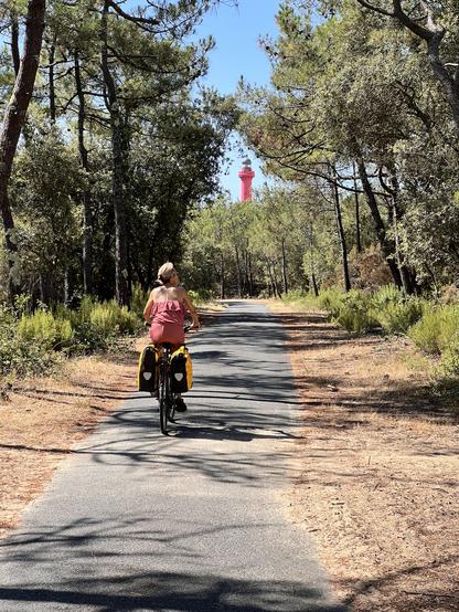 Bénédicte sur son vélo, dans la forêt , avec au fond, entre les pins, le phare de la Coubre