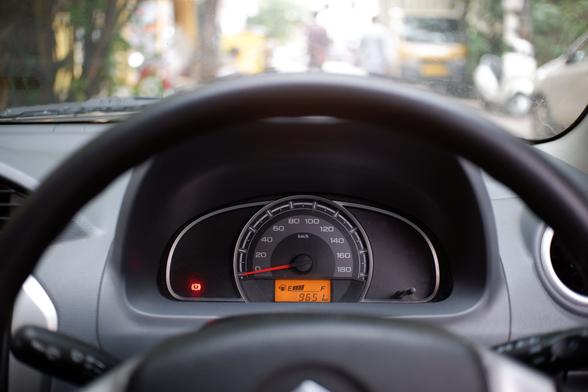 A steering wheel inside a car and a speedometer with the fuel indicator and a blurred background.
