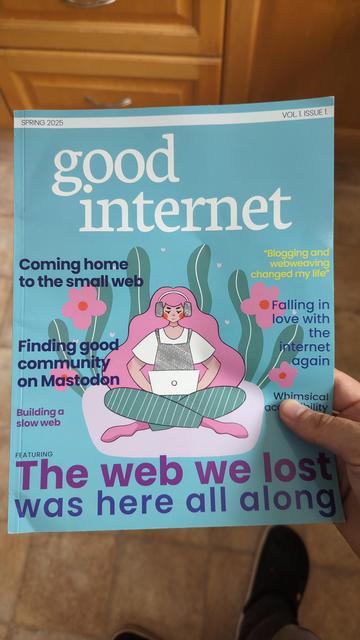 Photo of the blue cover of "good internet", an A4 magazine. It has cover art of someone sitting cross legged, using a laptop, while wearing headphones. The main title is "The web we lost was here all along".