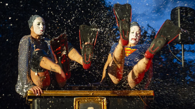 Photo du spectacle « Romeo+Juliette+Rose », par la compagnie C’est pas grave. Deux personnages portant un masque blanc, et chaussés de palmes, sont assis sur un bureau.