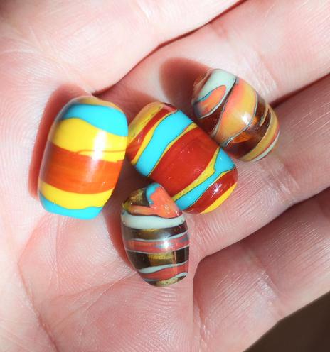 Image of several handmade lampwork glass beads in New Mexico colors of yellow, red and turquoise, resting in the palm of a hand,