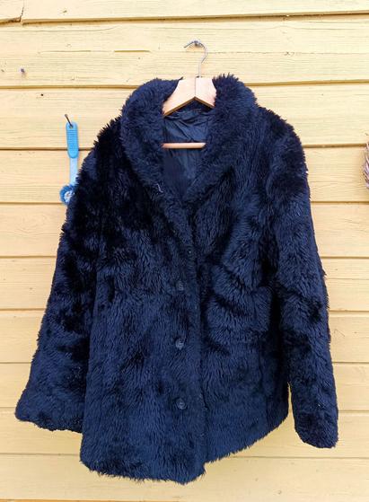A fluffy black synthetic fur coat with smooth black inner liner. It looks quite warm. There's four buttons and no pockets at all.