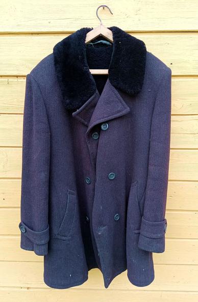 A thick woolen winter coat in dark gray, with a black faux fur collar, double button rows and straps at the sleeves. There's two pockets on the outside and one inside. It looks like what old blokes wear to funerals.