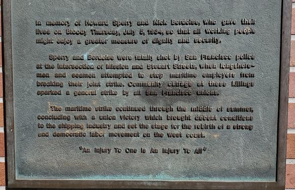 The plaque reads: 

“In memory of Howard Sperry and Nick Bordoise, who gave their lives on Bloody Thursday, July 5, 1934, so that all working people might enjoy a greater measure of dignity and security.

Sperry and Bordoise were fatally shot by San Francisco police at the intersection of Mission and Steuart Streets, when longshoremen and seamen attempted to stop maritime employers from breaking their joint strike. Community outrage at these killings sparked a General Strike by all San Francisco unions.

The maritime strike continued through the middle of the summer, concluding with a union victory which brought decent conditions to the shipping industry and set the stage for the rebirth of a strong and democratic labor movement on the west cost.

An Injury to One is an Injury to all.”