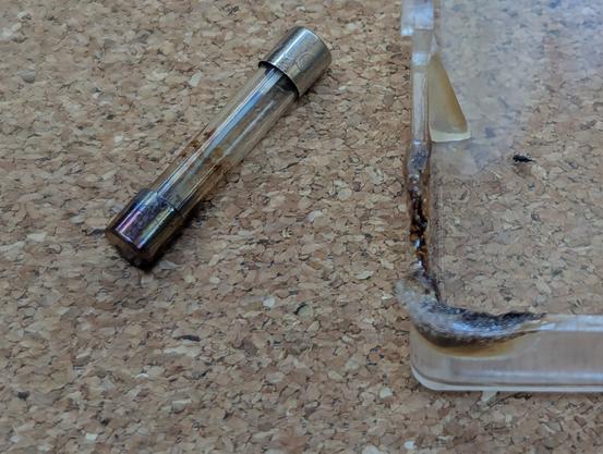 A classic glass fuse and part of the plastic fuse box cover. The corner of the cover is melted and the fuse is badly discolored.