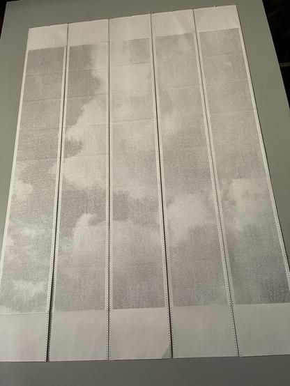 Five 10-page strips of continuous wide format computer paper hanging on a wall, viewed from below.
