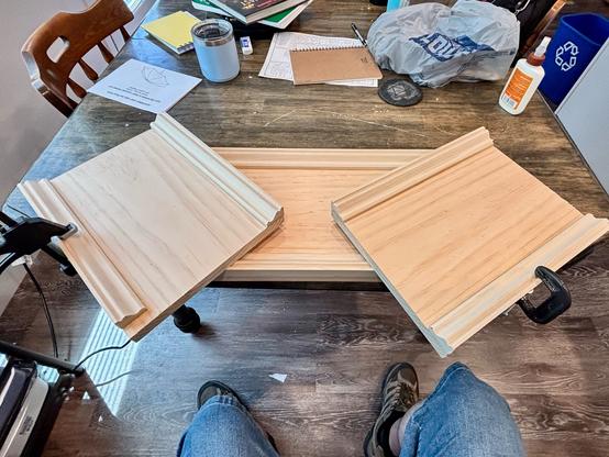 Three sections of wood on a table with glued on trim pieces. Two shorter sections have clamps holding the trim in place.