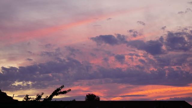 Hausdach, darüber Wolken in unterschiedlichen Farben