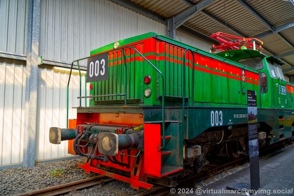 A photo of the front an electric locomotive painted in green with red stripes and the number 003 on the front and the side. It has the registration number 97 80 1200 003-7.