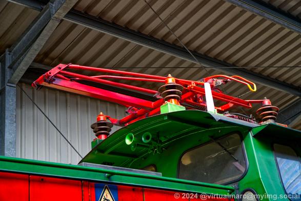 A close up detail photo of the pantograph of an electric train, painted in red.