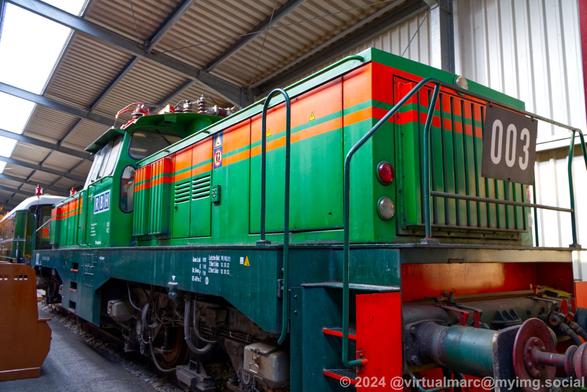 A photo of the back of an electric locomotive painted in green with red stripes and the number 003 at the back.
