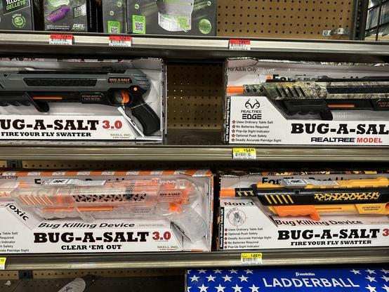 Retail shelf display showing four different colorways of a product called the "BUG-A-SALT 3.0": a plastic gun for shooting insects with table salt.

Top left: classic gray and black with orange highlights.
Top right: CAMO.
Bottom left: clear plastic.
Bottom right: Tonka-themed black and yellow.