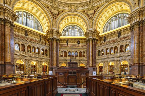 Interior view of the main reading room in the Jefferson building of the Library of Congress in Washington DC. The room is octagonal, with desks arranged in concentric circles and the circulation desk in the center of the room. It is 125 feet in height and the room is surrounded by eight large columns that support the arches beneath the dome. Above each of these columns is a 10 1/2-foot-tall plaster statue, with each representing a different branch of knowledge.