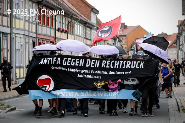 Die Demonstrant*innen auf der Westermarktstraße, ziehen in Richtung Autonomes Zentrum (AZ). Auf dem Frontbanner steht "Antifa gegen den Rechtsruck. Gemeinsam kämpfen gegen Faschismus, Rassismus und Antisemitismus!". Zudem ist eine Fahne der Antifaschistischen Aktion zu sehen, ebenso viele aufgepannte Regenschirme.