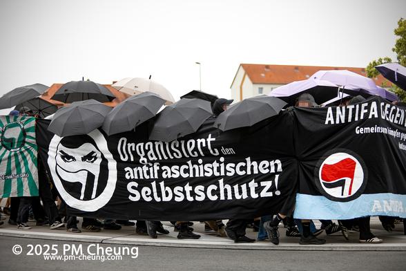 Ein weiteres Transparent mit der Aufschrift "Organisiert den antifaschistischen Selbstschutz!". Zudem sind auch hier viele aufgespannte Regenschirme zu sehen.