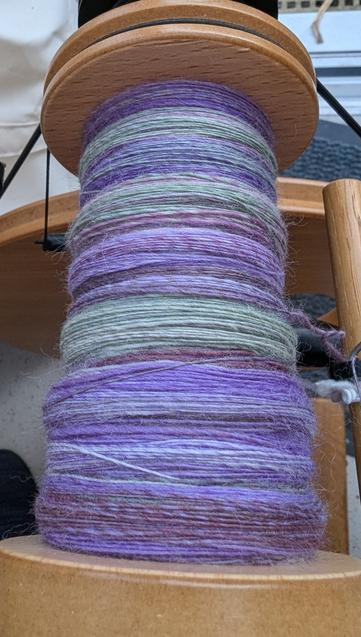 A part filled bobbin of handspun singles. The fibre is fine merino and the colour is called Lavender - shades of purple and dusky light green.