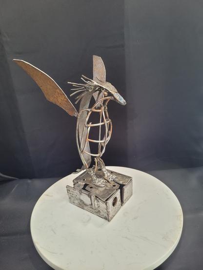 Un pingouin de type gorfou sauteur en acier recyclé se tient sur une banquise incomplète, qui en realite est un coffret. 

Les nageoires ainsi que le dos sont en acier rouillé. Le petit bedon est fait de grillage. Ses cheveux/plumage sont des clous.

La boîte est construite avec toute sorte de matériaux disparates et incomplets. Elle s'ouvre en faisant basculer le pingouin vers l'arrière.