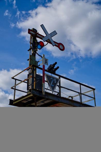 A photo of a railway form signal on a small bridge over the railway near a railway crossing.