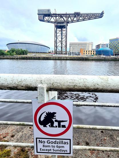 A sign showing Godzilla stamping on a building, with the building itself visible in the background. The sign reads No Godzillas 8am to 6pm Except Sundays.