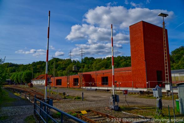 A photo of the big red brick building, that is the entrance building of the railway museum. In front you can see the railway crossing.