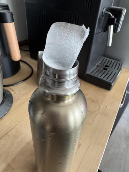 a metallic water bottle with an ice cube balanced near its opening. The cube is too big to fit inside the bottle.