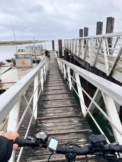 Sur la coursive d’un ponton, Tristan pousse son vélo. Devant, Benedicte pousse le sien et s’apprête à monter à bord.