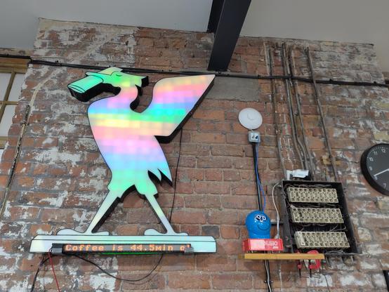 Rainbow illuminated Liver bird, connected bubble machine and sign saying how old the coffee is, on an industrial style brick wall