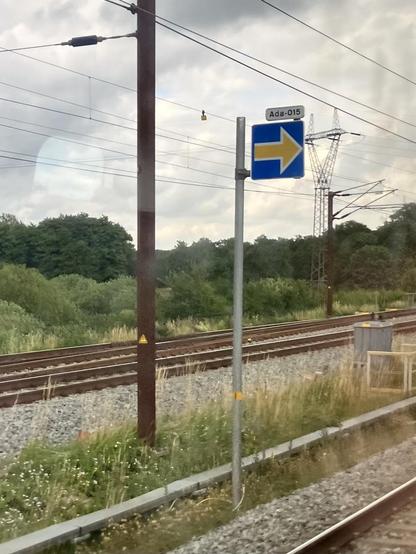 An ETCS Stop marker (a yellow arrow on a blue background pointing right) with a smaller sign above it that reads Ada-15 along some rails.