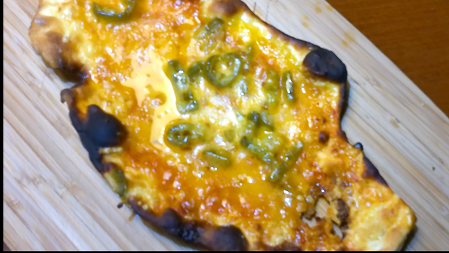 weirdly shaped homemade pizza with beautifully melted vegan cheese and charred bits on a bamboo board