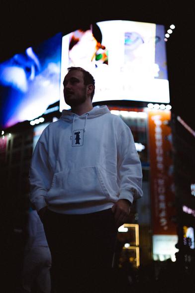 portrait of a man in a white hoodie in front of large bright billboards, photographed at night