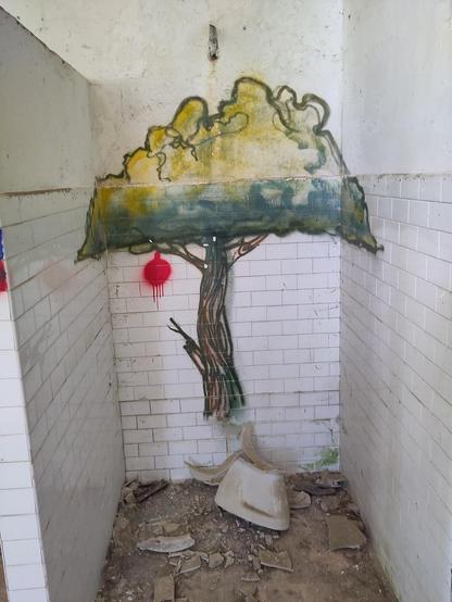 Un albero disegnato sulle mattonelle bianche dello stallo di un bagno, con la tazza divelta e calcinacci tutti intorno.