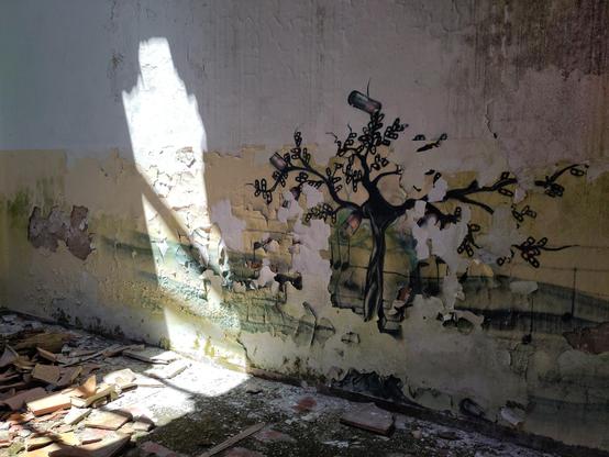 Un albero disegnato sulle mattonelle bianche dello stallo di un bagno, con la tazza divelta e calcinacci tutti intorno.