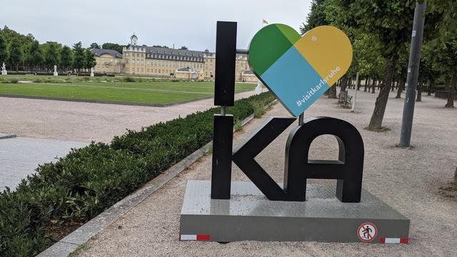 Ein I ❤️ KA Schriftzug mit den Karlsruher Schloss im Hintergrund. Im Herz steht der Hashtag #visitkarlsruhe