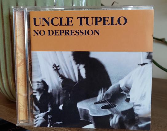 CD cover. The upper part is orange with band name and title in black.

Underneath, a black and white photo of the band with instruments. Snapshot-style, out of focus. The one closest has a guitar on his lap. Only a small part of his face is visible.
