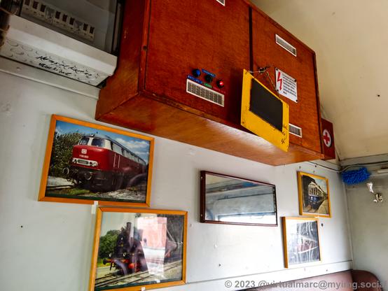 A photo of a wall inside a model railway with some fuses and an electrical cabin. There are photos of trains on the wall, including a steam train and a diesel  V160 train.