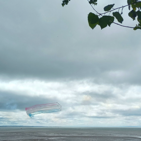 9 Red Arrows flying over Swansea Bay, trailing red, white, and blue smoke trails with an unfortunately cloudy background.