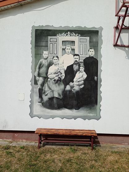 Mural we wsi Trześcianka na budynku remizy. Jest odwzorowaniem zdjęcia i przedstawia rodzinę: dwoje dorosłych i pięcioro dzieci. Rodzice siedzą, matka trzyma dziecko w ramionach, ojciec na kolanie, pozostała trójka stoi za rodzicami. Pozują na tle ozdobnego okna z otwartą zdobioną okiennicą. Całość czarno-biała. U dołu drewniana ławeczka.