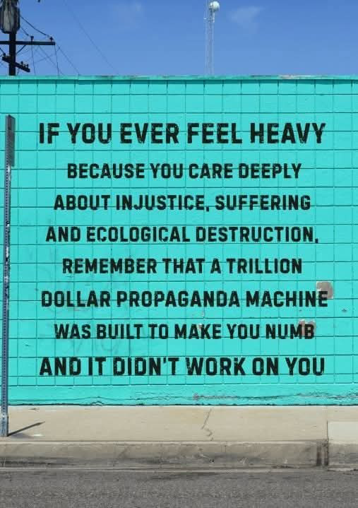 If you ever feel heavy because you care deeply about injustice, suffering and ecological destruction, remember that a trillion dollar propaganda machine was built to make you numb and it didn't work on you Words on an aqua colored outside wall