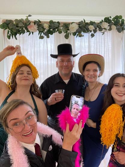 Myself, my partner and my cousins, in goofy costumes. The one cousin who couldn't make it is on FaceTime on a phone, with boa wrapped around the phone.