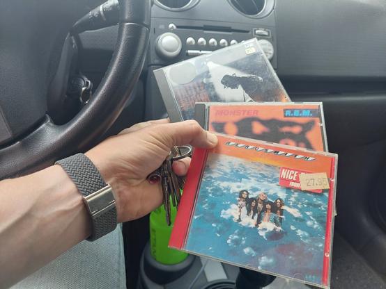 Drie albums op CD in รฉรฉn hand: Rattle and the Hum van U2, Monster van REM en Aerosmith van Aerosmith