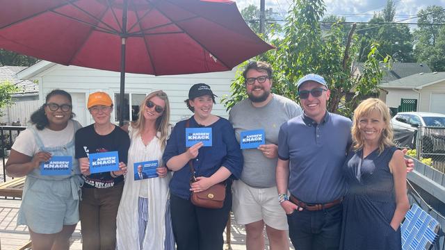 Andrew standing with a group of people. Some people are standing under and umbrella and others are holding up a card that says Andrew Knack for Mayor.