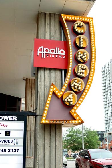 Photo taken outside of the Apollo Cinema's lit-up "CINEMA" sign in the shape of a large red arrow.