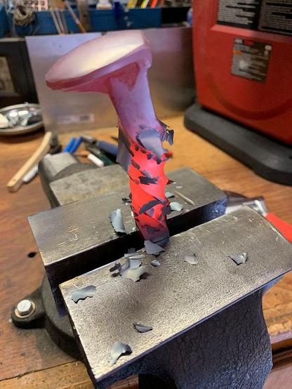 A hot railroad spike in a small mechanic's bench vise has been twisted, resulting in forge scale breaking off from the surface.