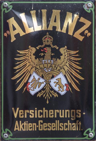Old sign of "Allianz Versicherungs Aktien Gesellschaft" ("Alliance Insurance public limited") - gold on black, with a an eagle in the middle. The eagle has a crown, and holds some shields / coat of arms.