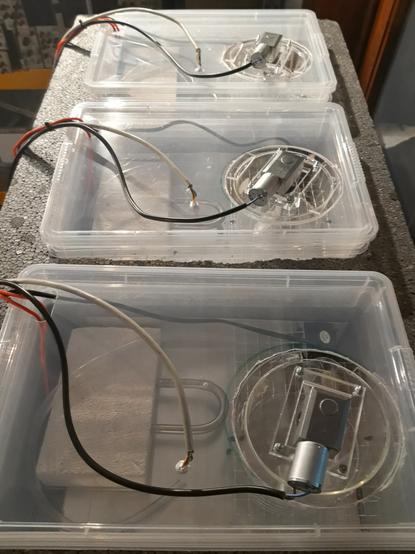 Three plastic reservoirs embedded in polystyrene isolation. Each reservoir has the same arrangement of parts and the same cables running down from it on the left side of the image. Through the lid a heating element can be seen in each reservoir, on the lid of each reservoir is an electromotor and a simple mechanism assembled out of  perspex parts.
